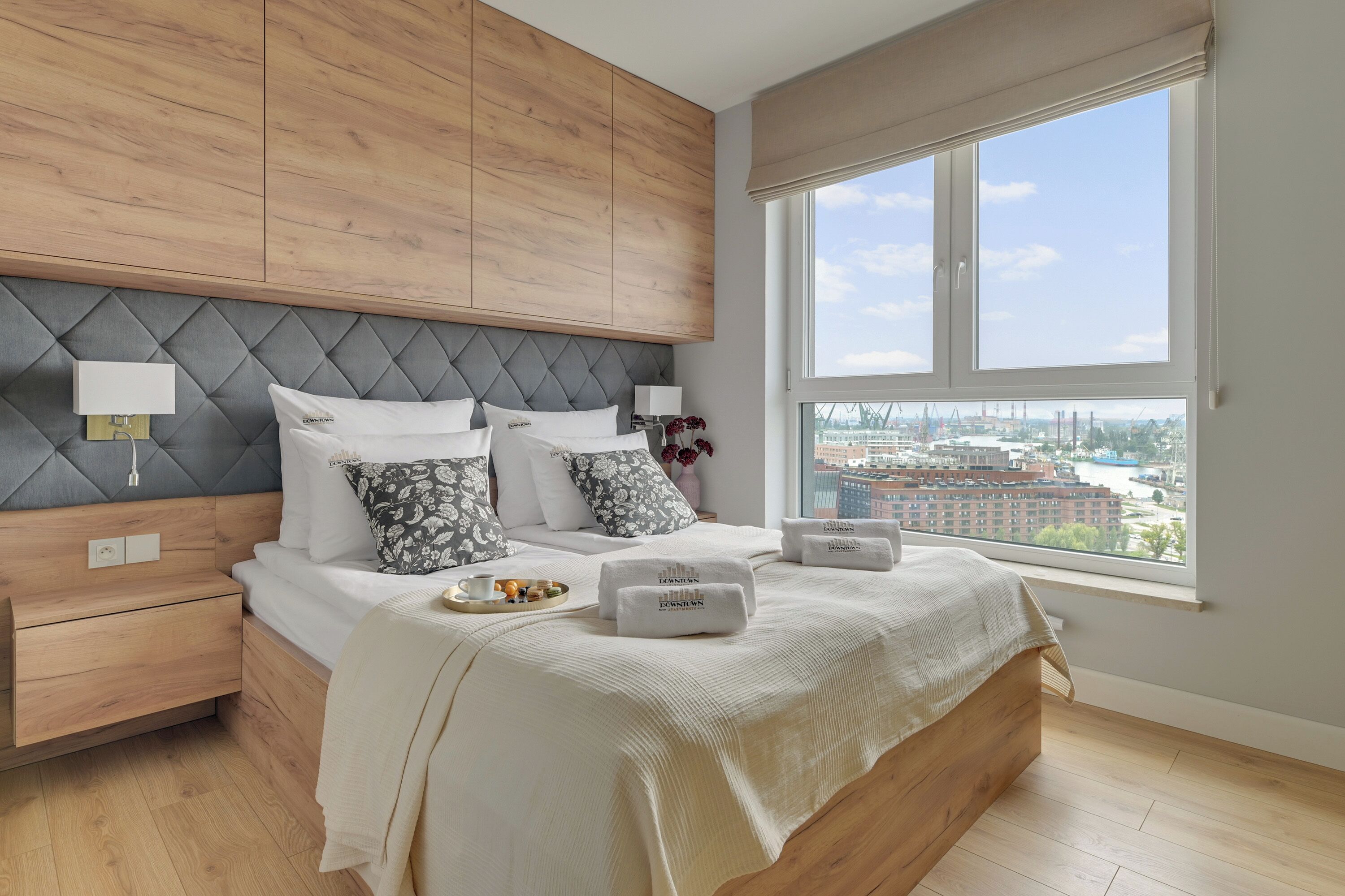 Ein modernes Schlafzimmer mit einem großen Bett, einem Nachttisch, einer Kommode und einem Fenster mit Blick auf die Stadt.