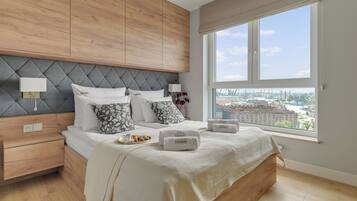 Un dormitorio moderno con una cama grande, una mesita de noche, un tocador y una ventana con vista a la ciudad.