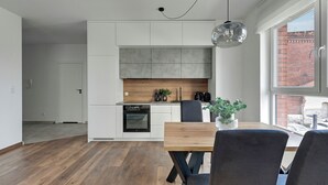 A modern kitchen with white cabinets, a wooden countertop, and a built-in oven. There is a dining table with chairs and a hanging light fixture. -  Bastion Wałowa City Center & Parking by Downtown Apartments (Gdansk)
