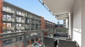 A balcony with wicker furniture, a glass railing, and a view of adjacent buildings. -  Bastion Wałowa City Center & Parking by Downtown Apartments (Gdansk)