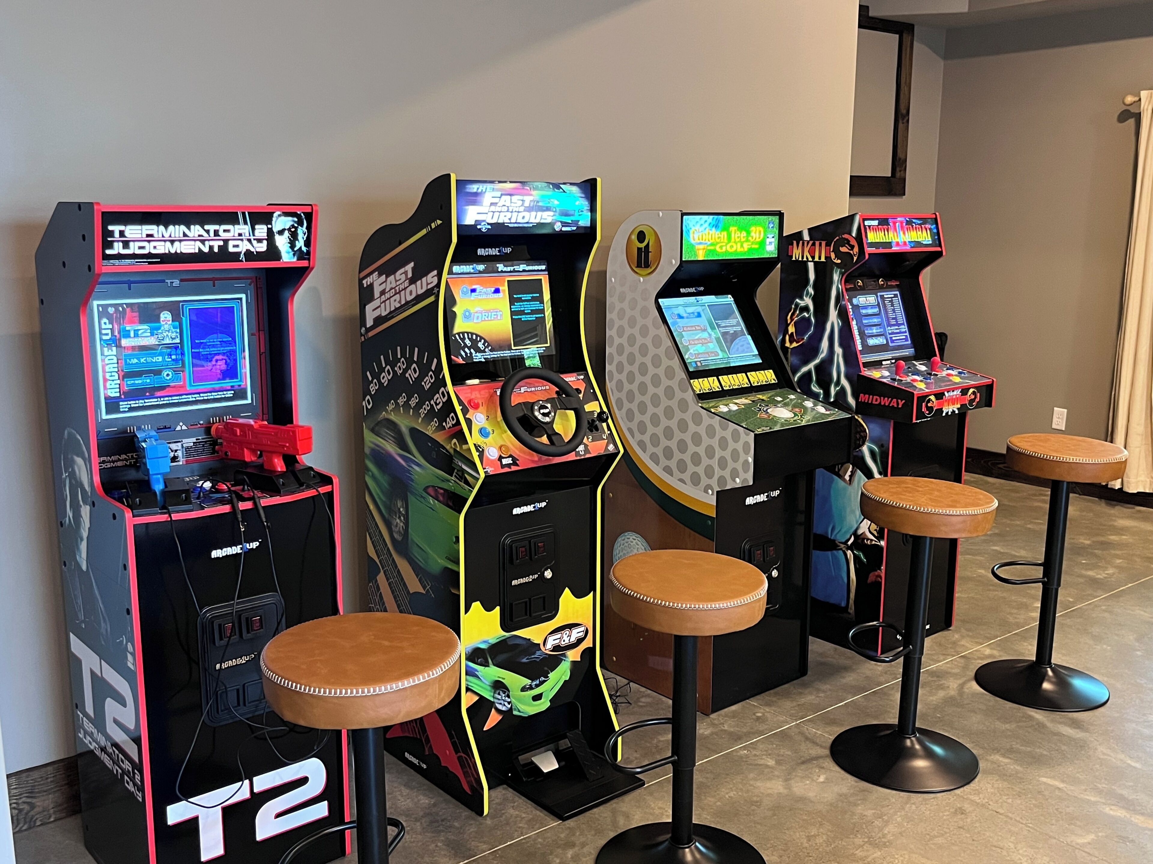 Four arcade machines with racing games, each with a unique theme, and two stools in front of them.