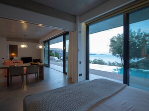 Een moderne hotelkamer met een groot bed, een zithoek met een tafel en stoelen, en uitzicht op de zee door grote ramen.
