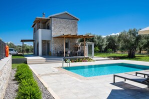 Et moderne hus i to etager med swimmingpool, udendørs møbler og have.