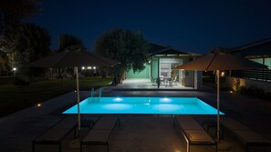Una piscina al aire libre con zona de patio, sillones de descanso y sombrillas.