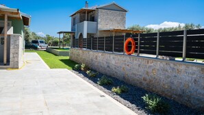 A modern house with a stone exterior, a fenced yard, and a clear blue sky.
