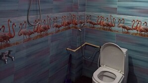 A bathroom with pink walls, a shower, a toilet, and a window with a fan. - Indralok Hotel By GRB (Jakholi)