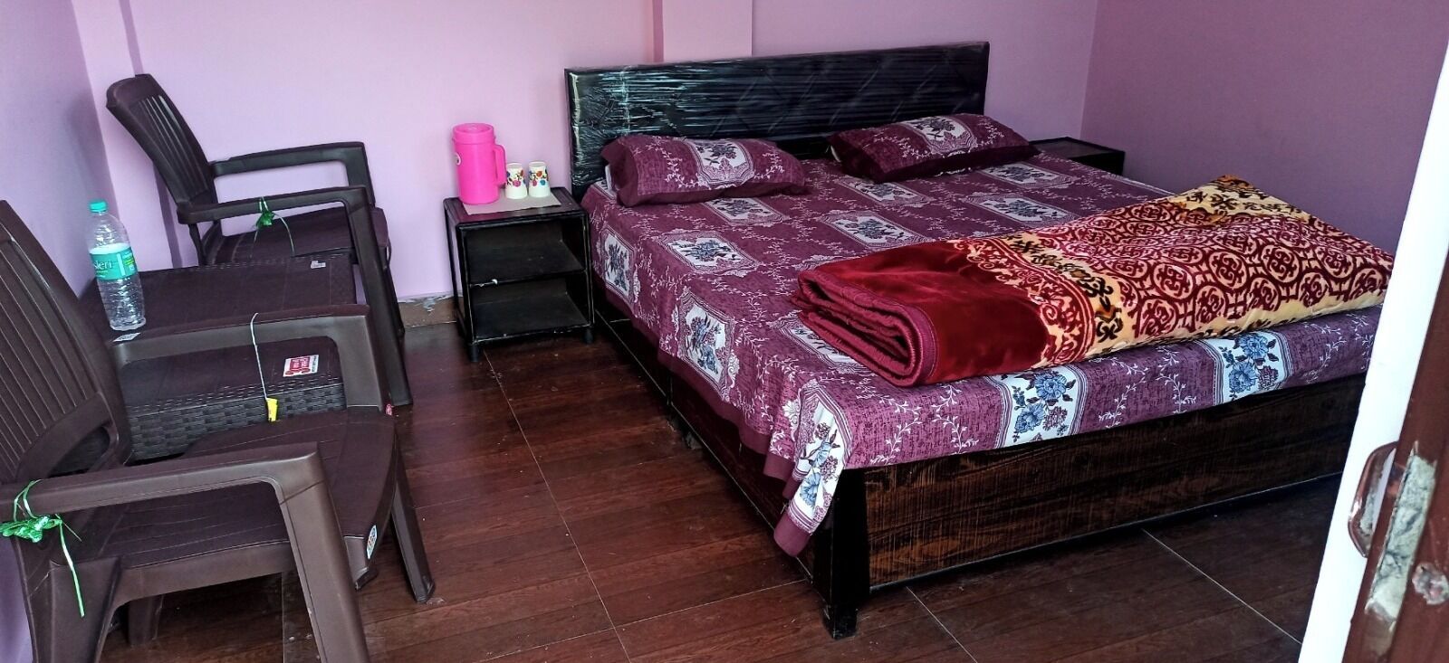 Une chambre avec un lit en bois, une table de chevet, une chaise et une bouteille d’eau.