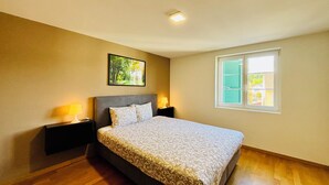 A bedroom with a bed, two bedside tables, a night lamp, a framed picture on the wall, and a window with shutters. - TONIGHT Apartments (Bottmingen)