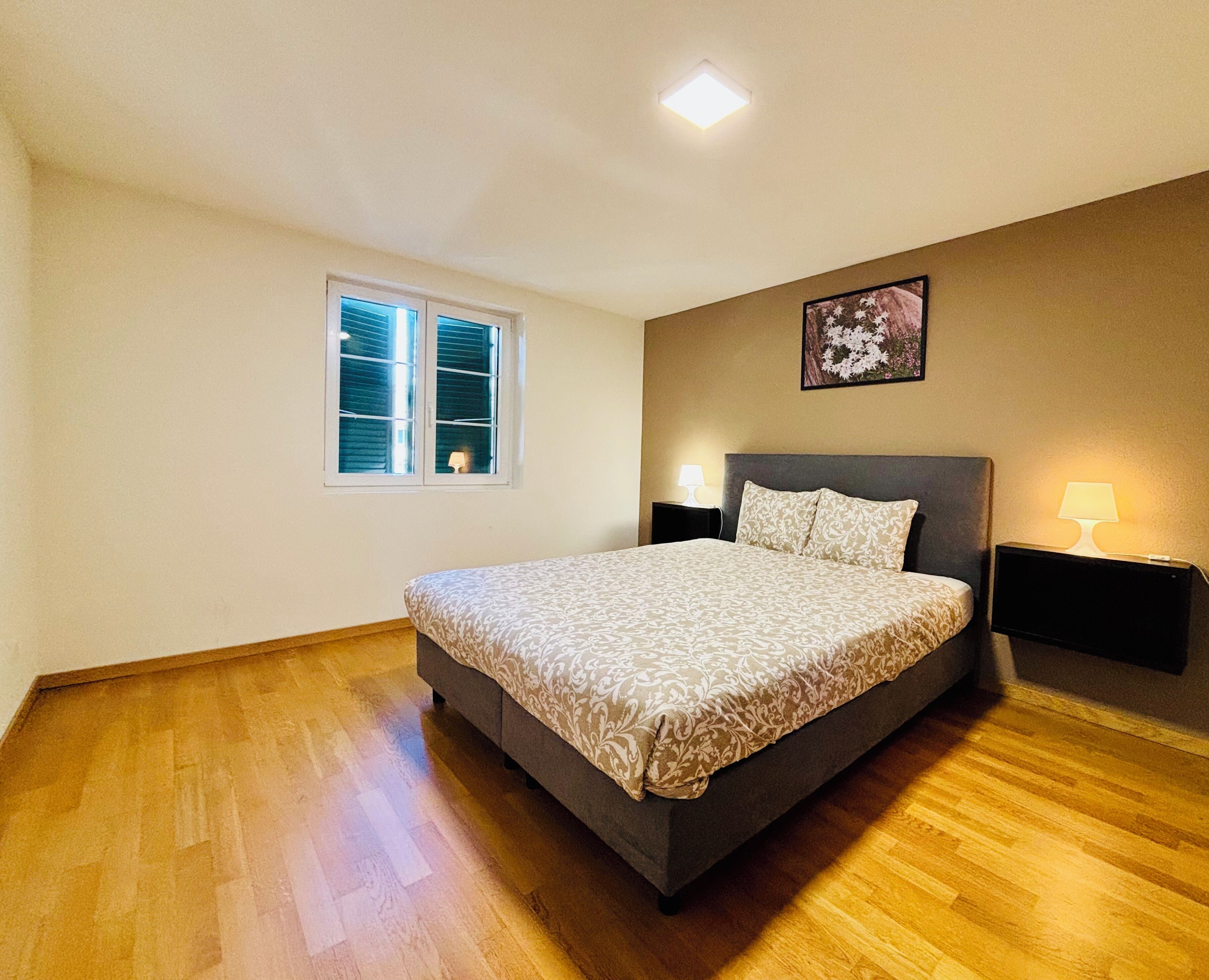 A bedroom with a bed, a window, a nightstand, and a wall-mounted lamp.