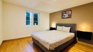 A bedroom with a bed, a window, a nightstand, and a wall-mounted lamp.