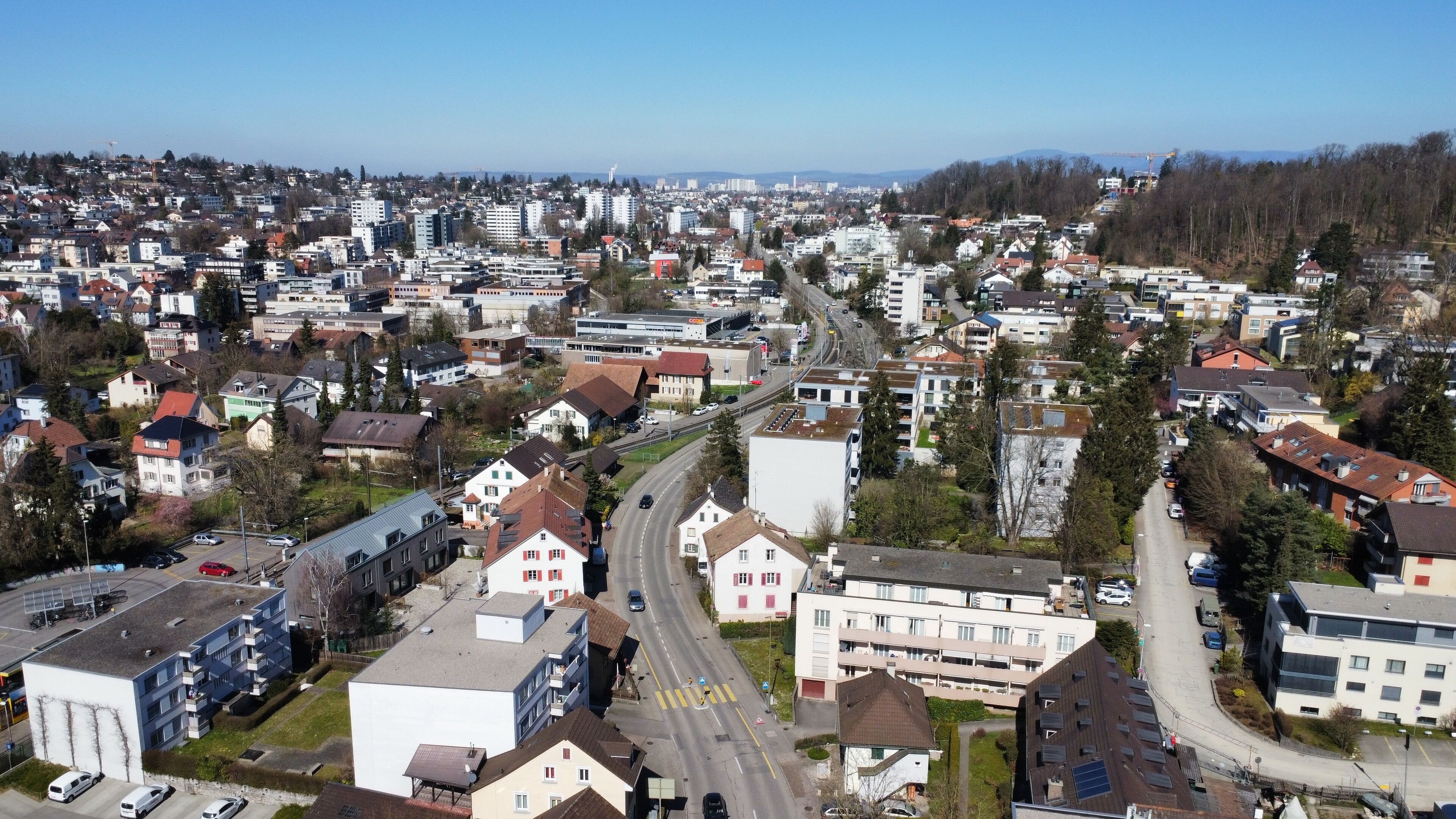 Een woonwijk met een combinatie van appartementencomplexen en huizen, met een hoofdstraat waar voertuigen rijden en voetgangersoversteekplaatsen zijn.