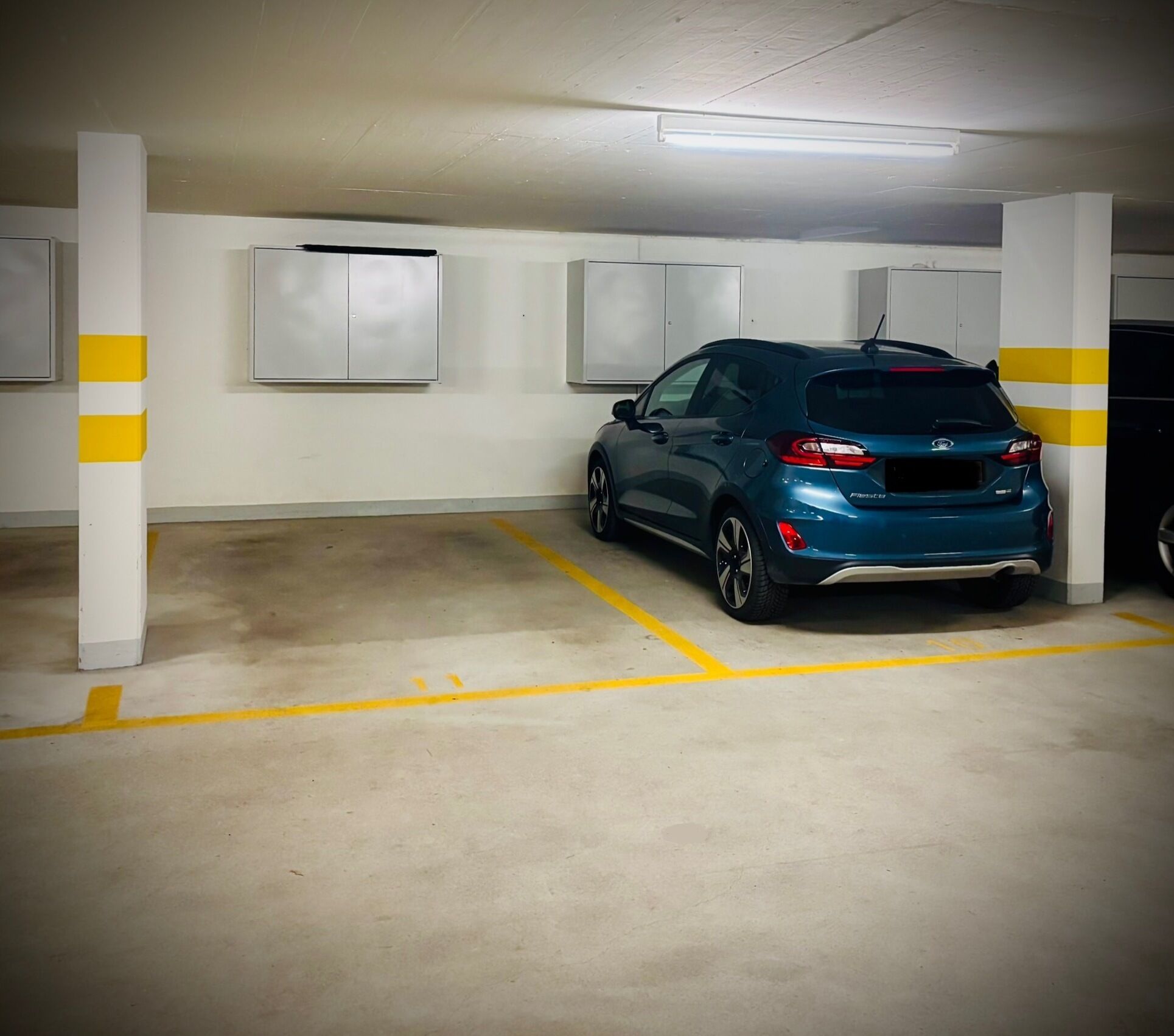 Un parking où une voiture bleue est garée dans un espace délimité par des lignes jaunes.