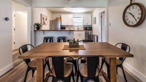 A dining area with a wooden table and black chairs, a ceiling fan, and a kitchen in the background. - The Azure Escape Summ (Corpus Christi)