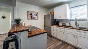 A modern kitchen with white cabinets, a wooden countertop, a stainless steel refrigerator, and a coffee maker. - The Azure Escape Summ (Corpus Christi)