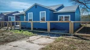 A row of blue single-story houses with white trim, wooden fences, and a clear sky. - The Azure Escape Summ (Corpus Christi)