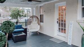 A covered porch with a wicker sofa, a white chair, and a welcome sign. - Park House - a Blackhouse Property (Tallahassee)