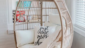 A white brick wall with a white wicker chair with a cushion and a pillow that says "Just done more." - Park House - a Blackhouse Property (Tallahassee)