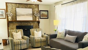 A living room with striped armchairs, a sofa, a fireplace, and framed artwork on the walls. - 3-Bdrm Home on Large Property at Norris Lake. Pet Friendly! (New Tazewell)