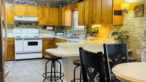 A kitchen with wooden cabinets, a white stove, and a dining area with a table and chairs. - 3-Bdrm Home on Large Property at Norris Lake. Pet Friendly! (New Tazewell)