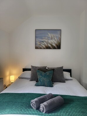Restful retreat with a neatly made bed, featuring a white duvet and a leaf-patterned pillow.