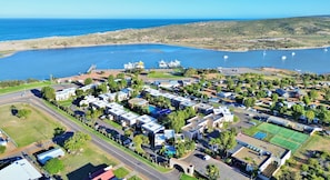 Eine Luftaufnahme eines Küstenresorts mit mehreren bungalowsartigen Unterkünften, einem Jachthafen und einem Sportplatz.