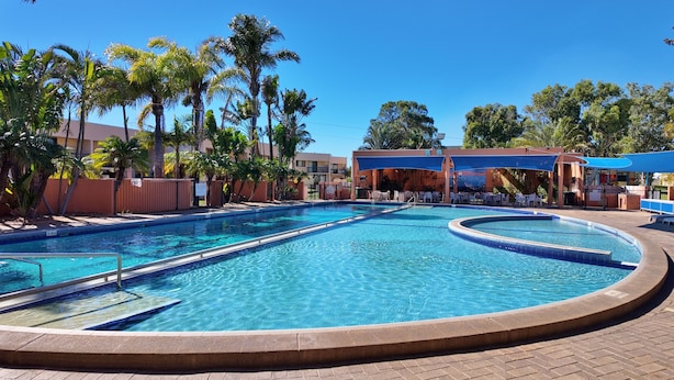 Une piscine au design incurvé, entourée de palmiers et dotée d’un espace détente abrité.