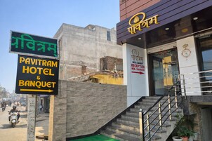 Entrada de un hotel con un mostrador de recepción, una escalera y un cartel que dice 'Pavitram Hotel & Banquet'.