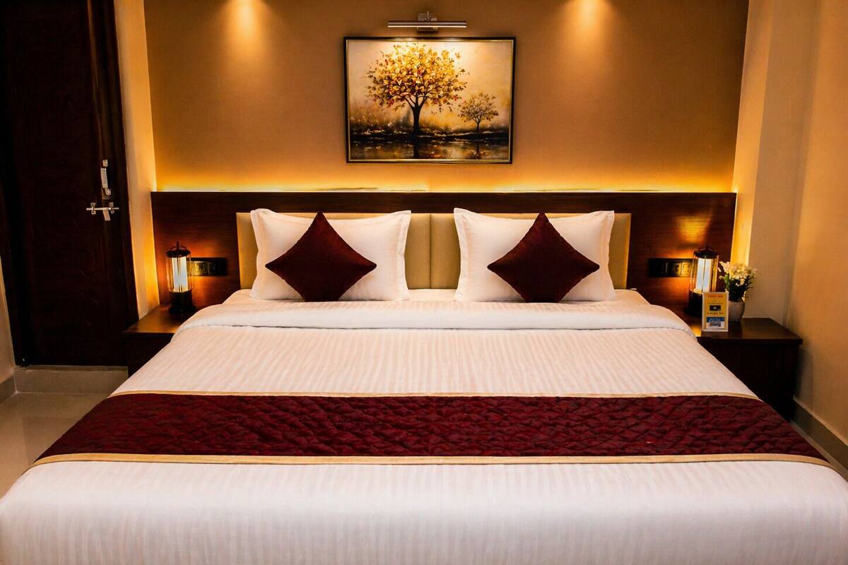 Habitación de hotel con una cama grande, dos mesitas de noche, una lámpara de pared y un cuadro de un árbol.