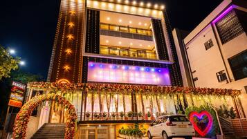 A multi-story building with a balcony, a signboard, and a car parked in front.