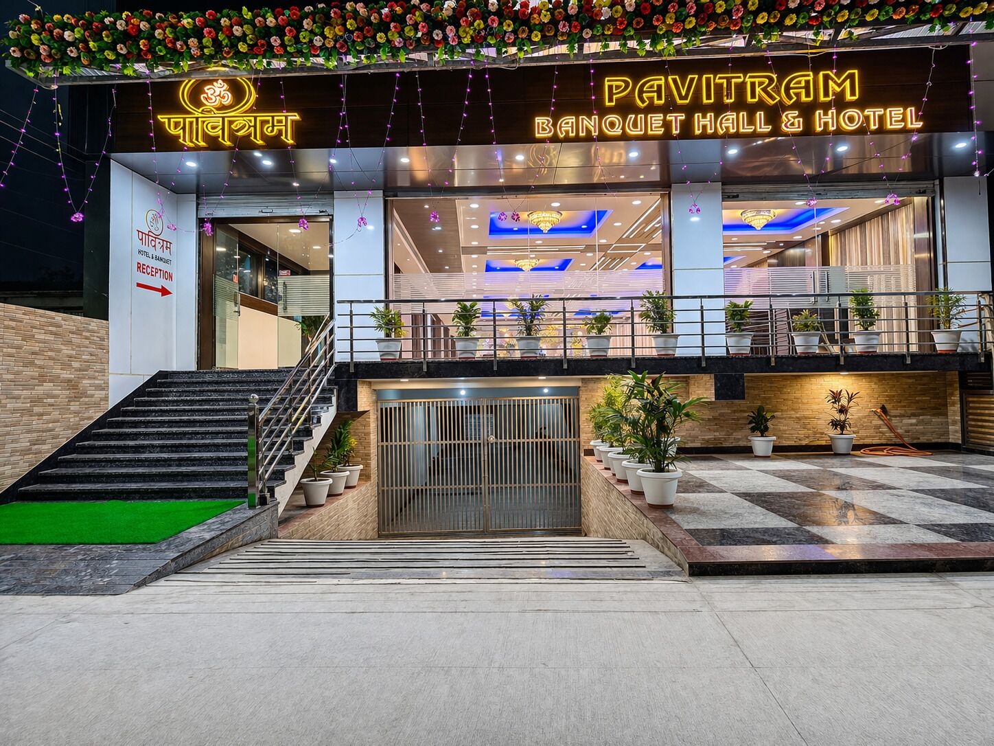 A hotel entrance with a reception desk, a staircase, and a balcony with potted plants.