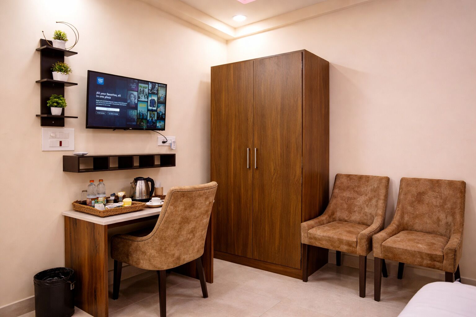 A room with a wooden wardrobe, a desk with a chair, a television, and two additional chairs.