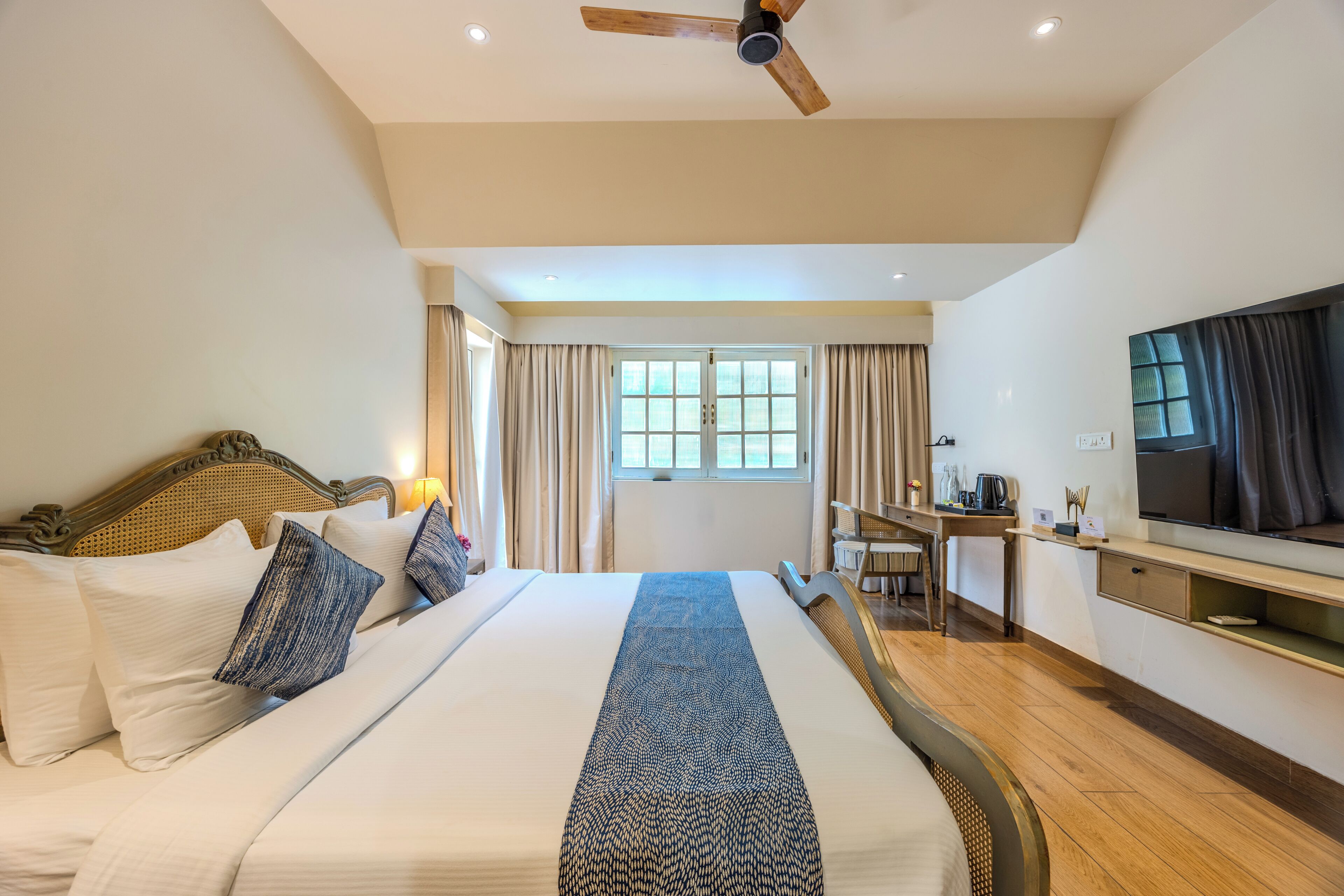 Una habitación de hotel con cama, escritorio, televisor y ventana con cortinas.