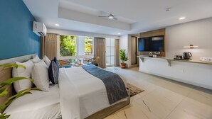 Une chambre d’hôtel moderne dotée d’un grand lit, d’une télévision, d’un petit coin cuisine et d’un balcon avec des rideaux.