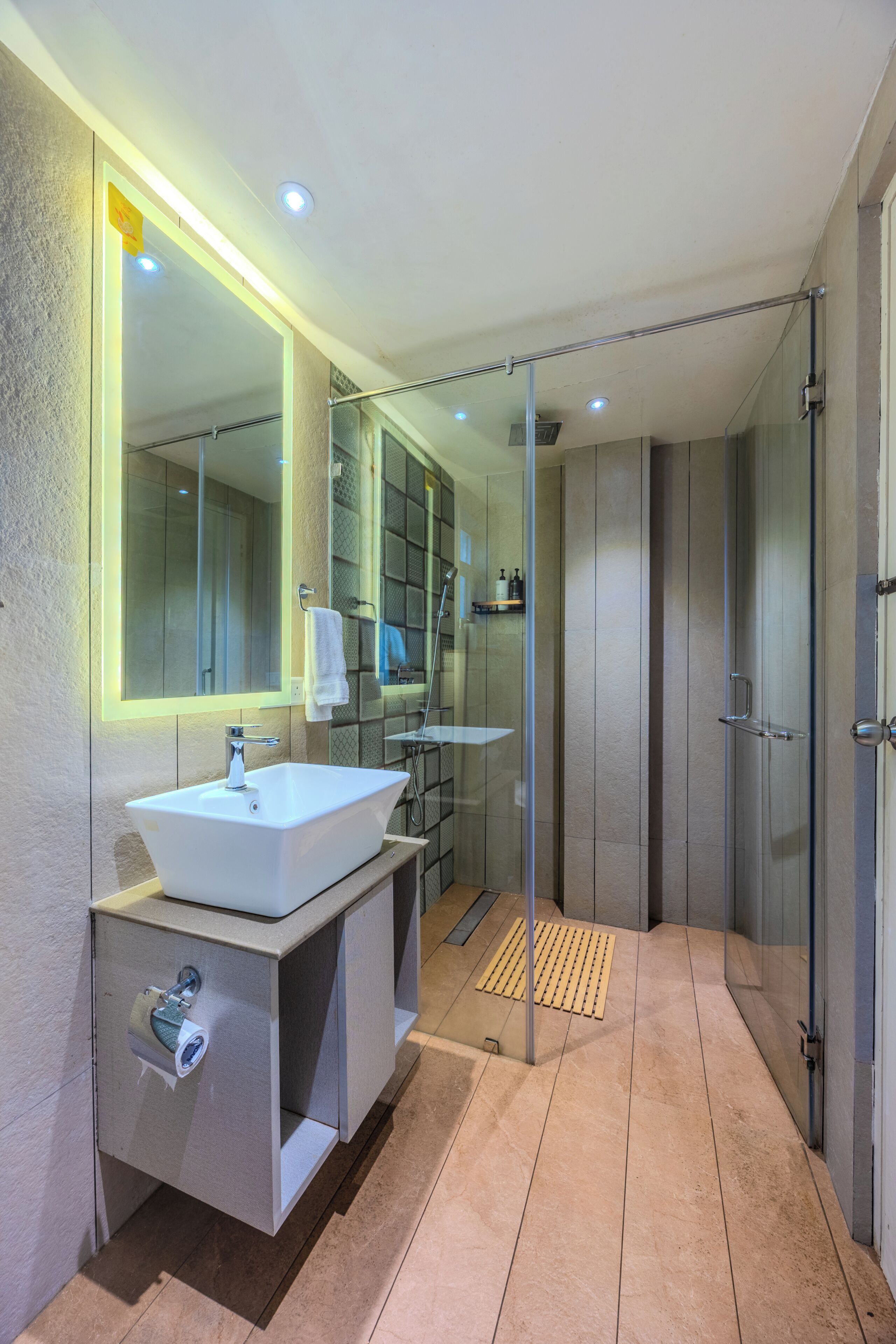 Un baño moderno con ducha de vidrio, lavamanos blanco y un espejo grande.