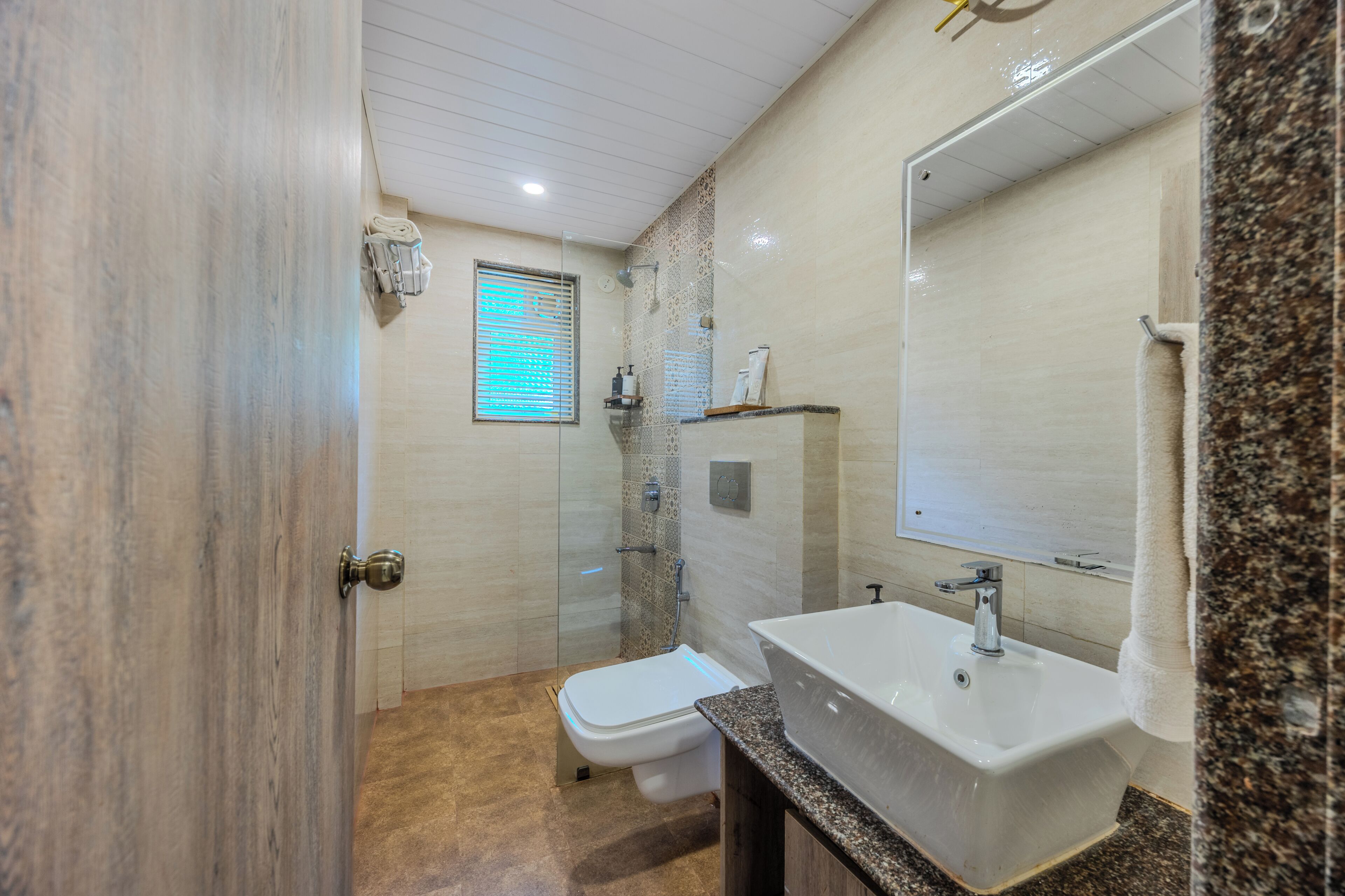 A bathroom with a shower, toilet, sink, and a large mirror.