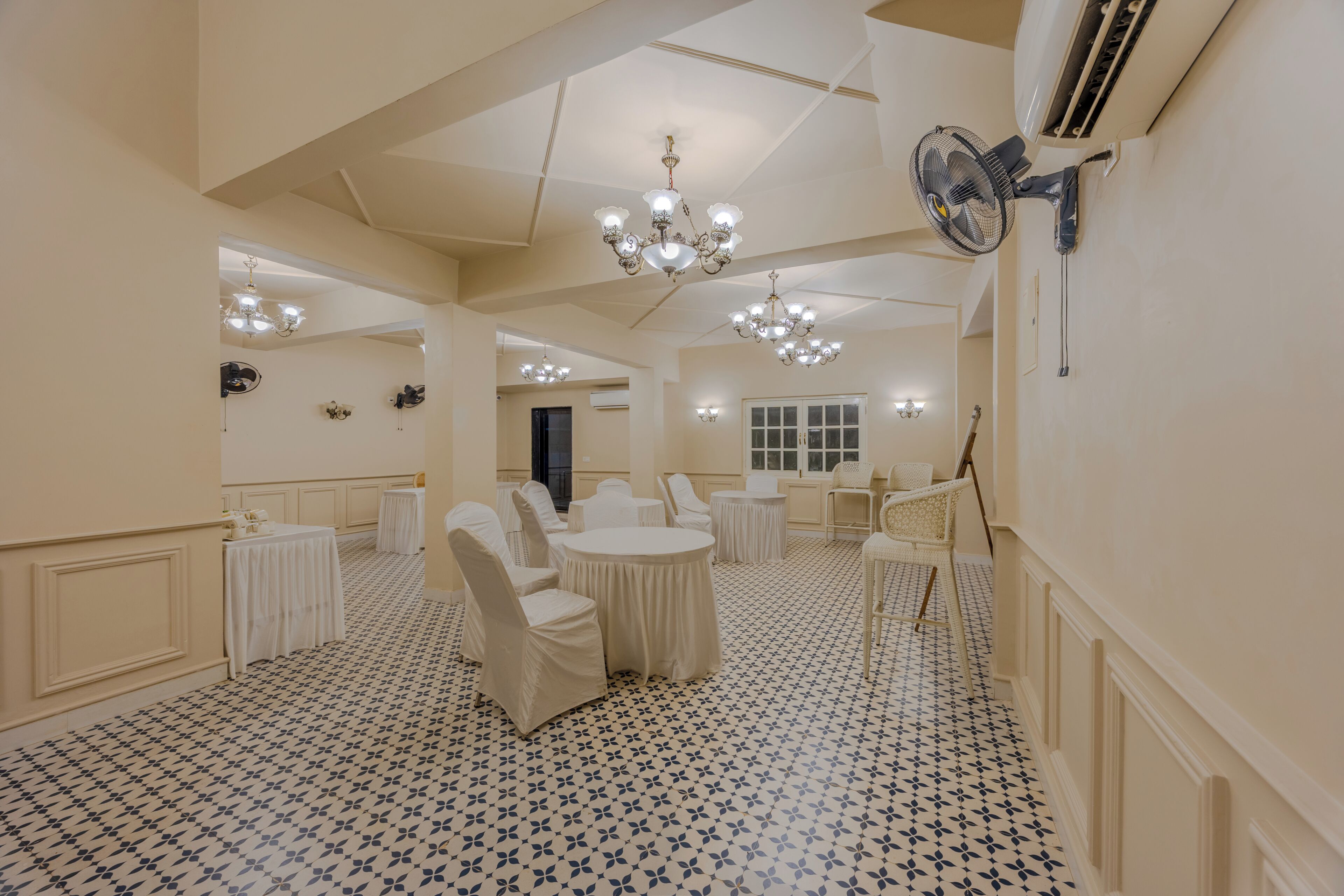 Um quarto com piso estampado, mesas redondas, cadeiras e um candelabro.