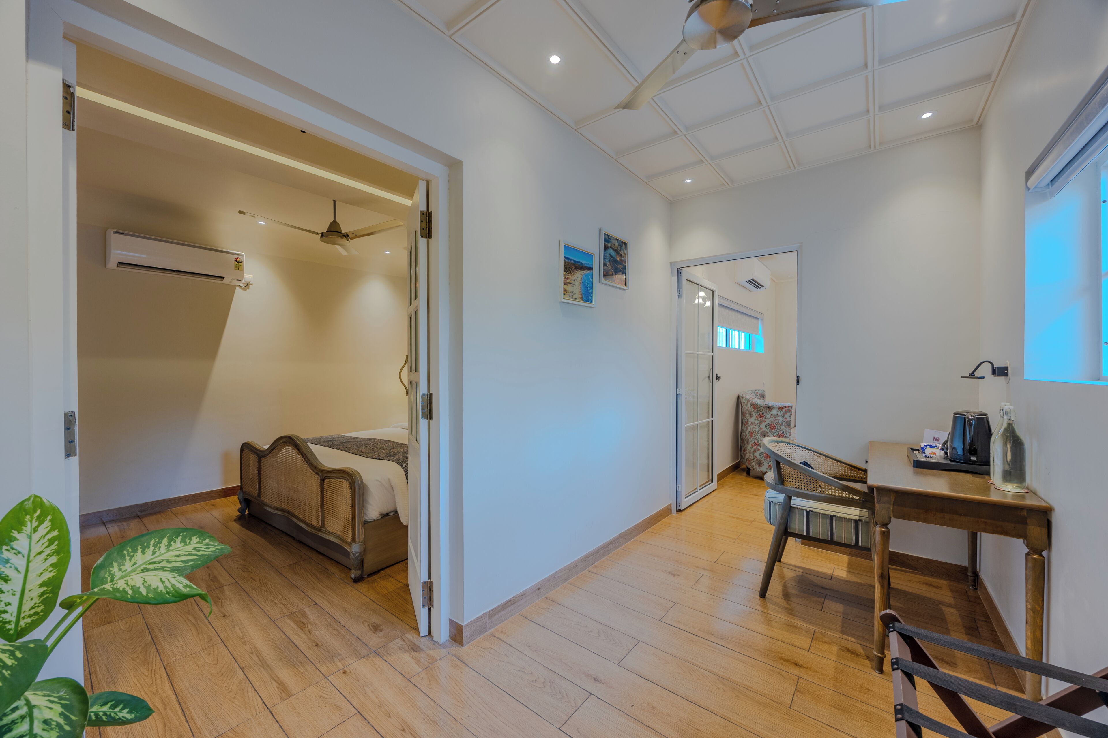 A room with a bed, a ceiling fan, a table with a kettle, and a window.