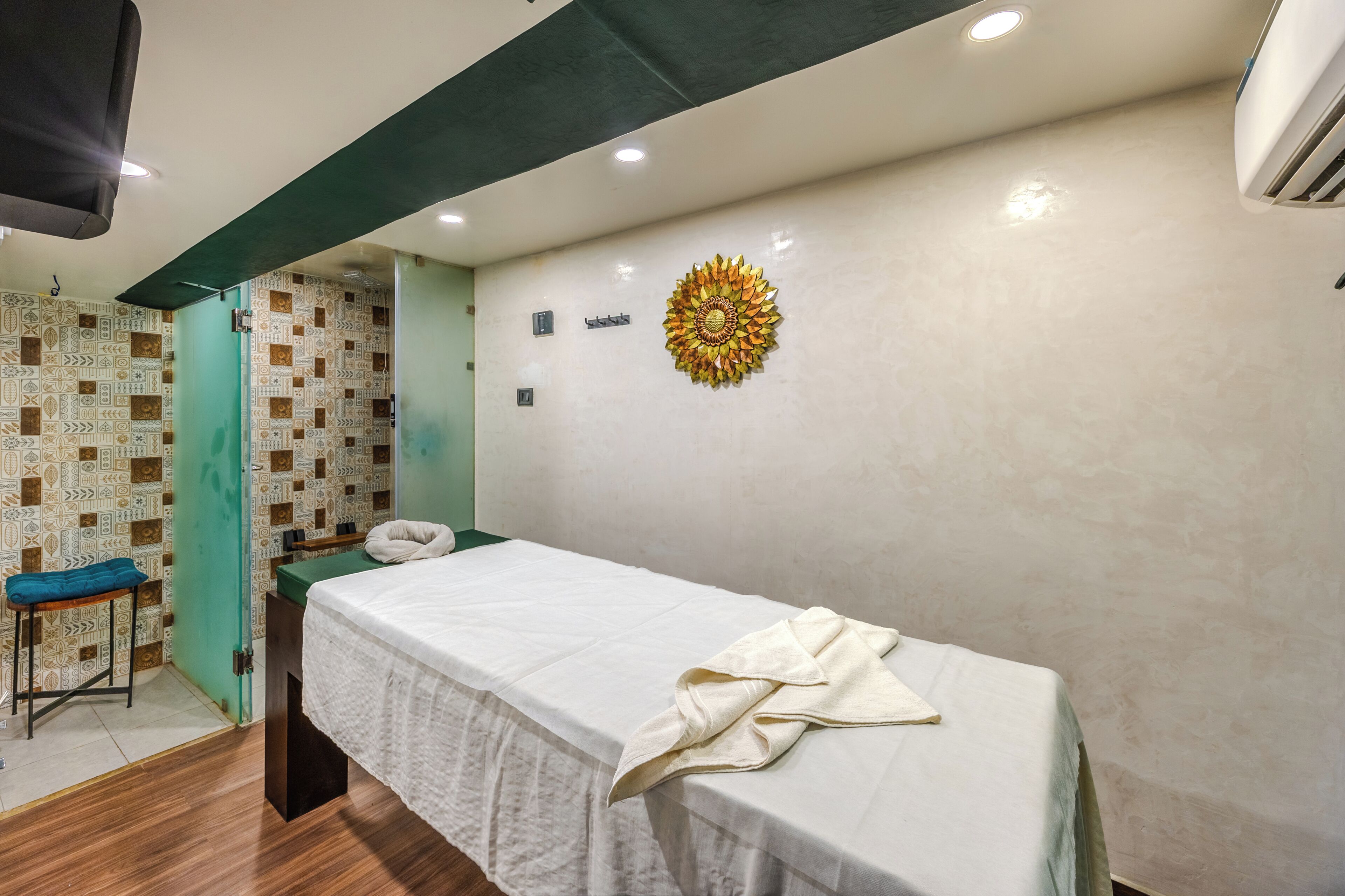 A room with a massage table, a stool, a wall with a decorative sunburst, and a patterned wall.