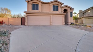 Una casa de dos pisos con fachada color beige, un garaje y un camino de entrada pavimentado.
