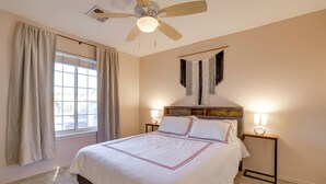 Un dormitorio con una cama grande, dos lámparas de noche, un ventilador de techo y una ventana con cortinas.