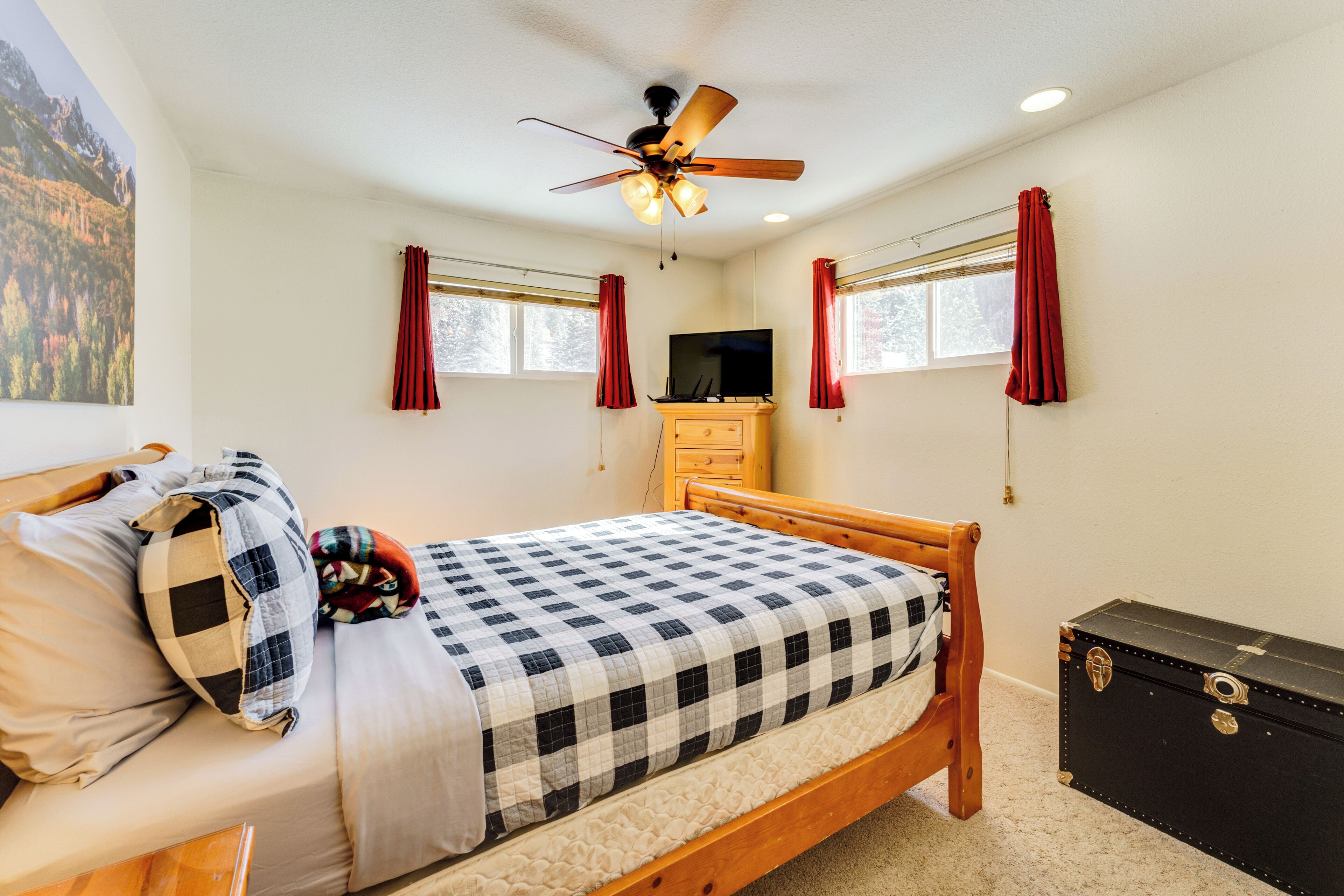 A bedroom with a bed, a wooden dresser, a ceiling fan, and a window with curtains.