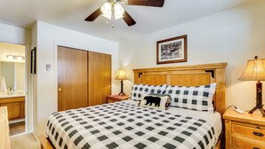 Quarto com cama, cabeceira de madeira, mesa de cabeceira, abajur e ventilador de teto.