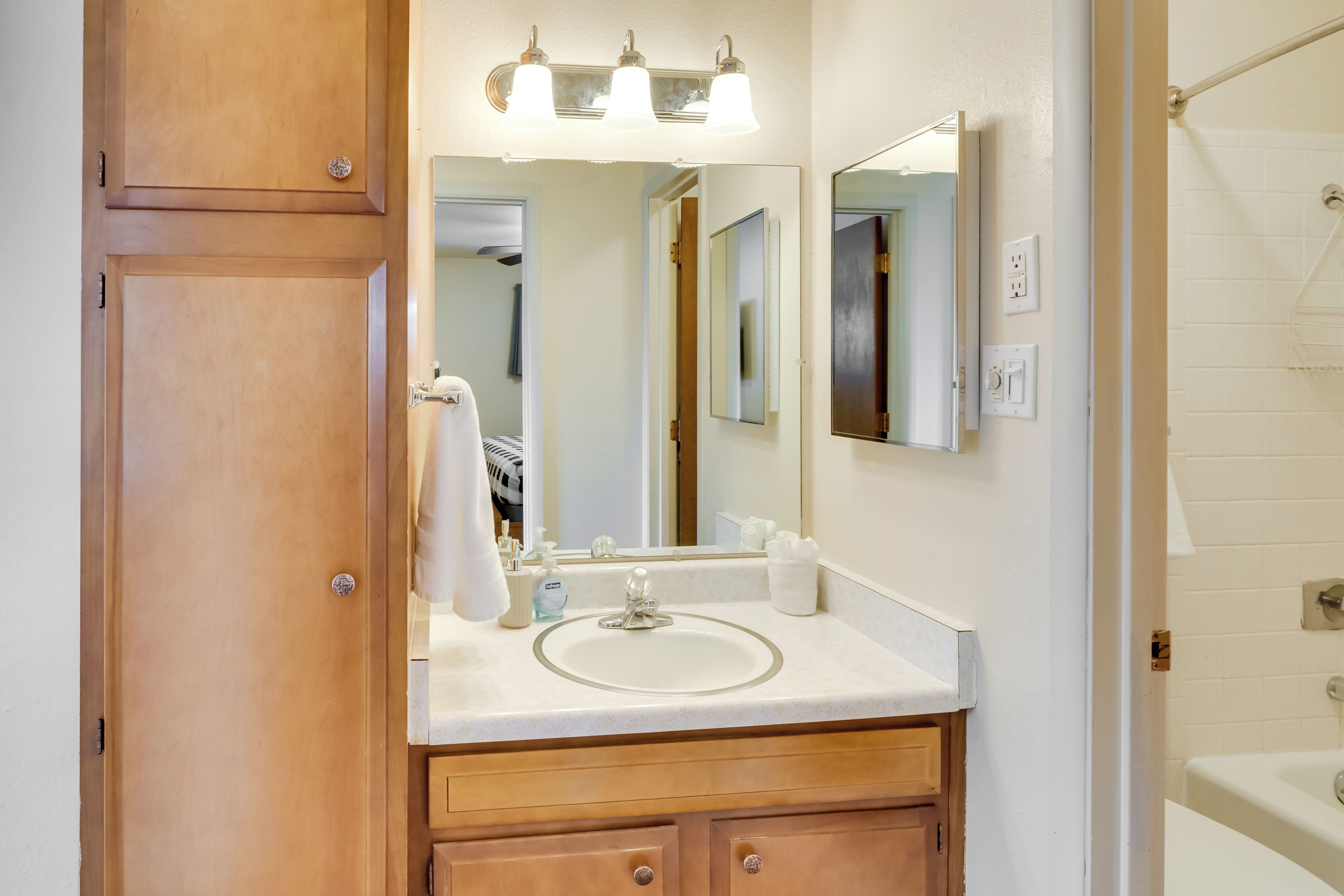 A bathroom with a wooden vanity, a sink, a mirror, and a shower area.