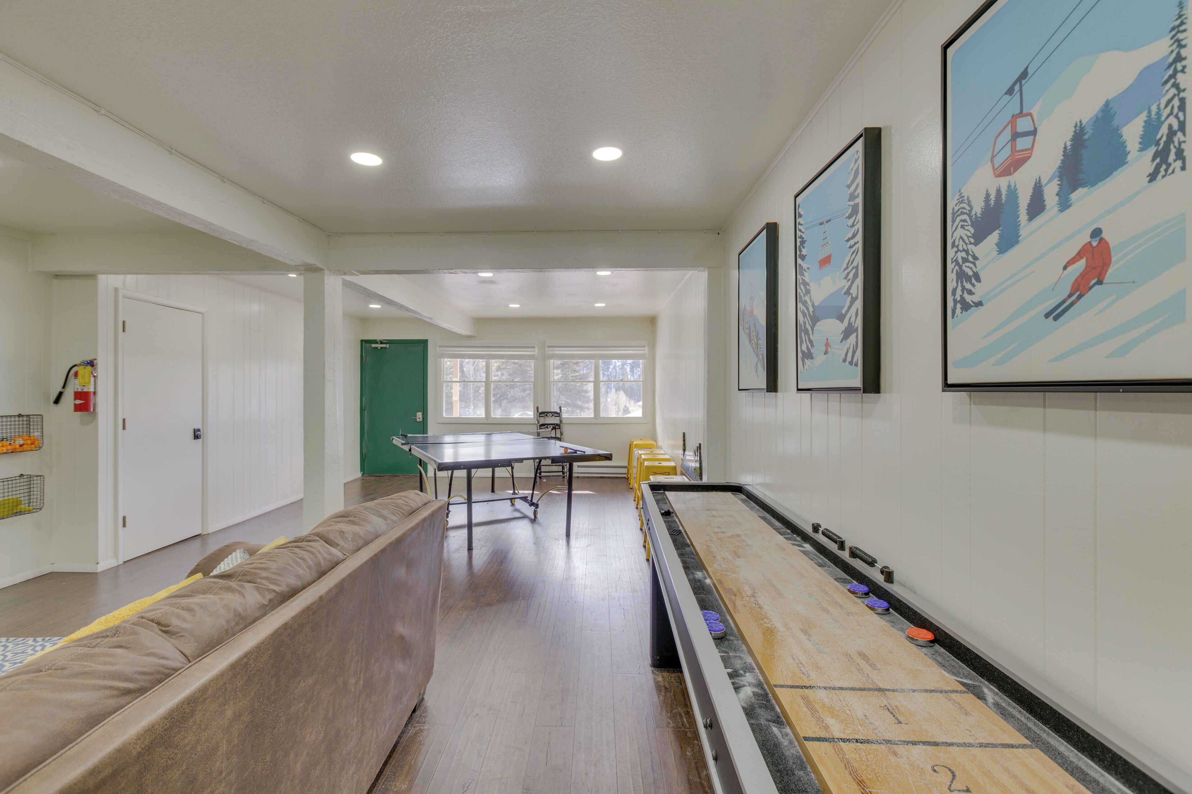 A room with a shuffleboard table, a long couch, and a green door.