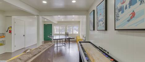 A room with a shuffleboard table, a long couch, and a green door.