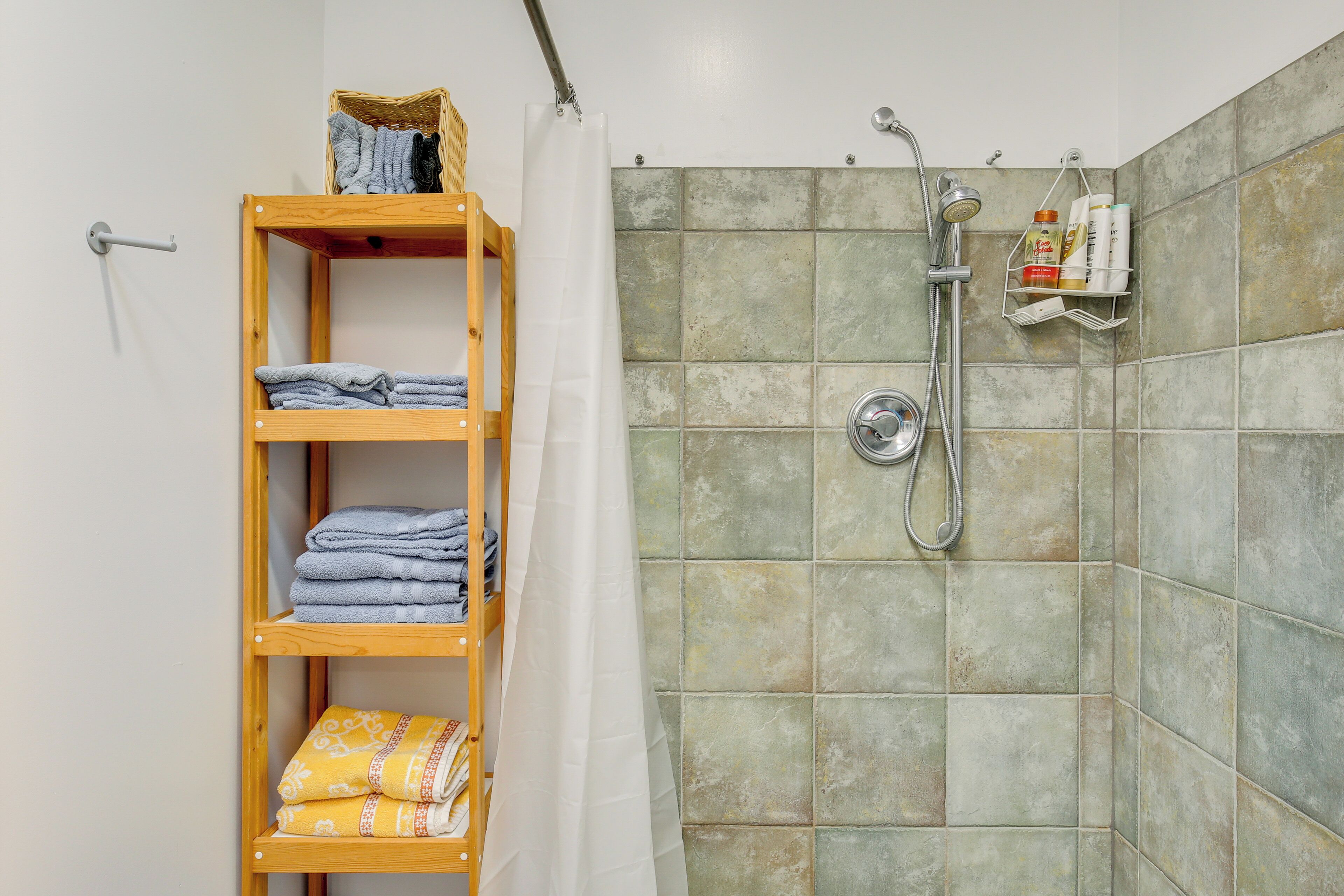 A shower area with a tiled wall, a wooden shelf with towels, and a showerhead.