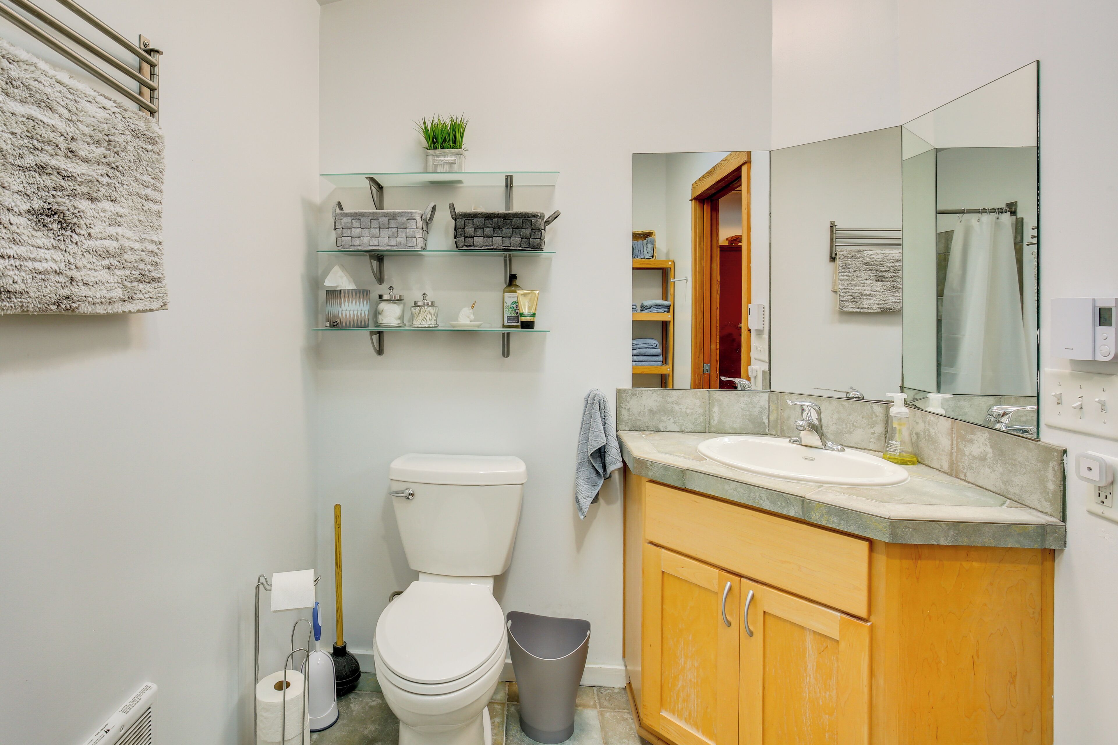 A compact bathroom with a toilet, a sink, and a mirror. There are shelves above the toilet and a towel rack on the wall.