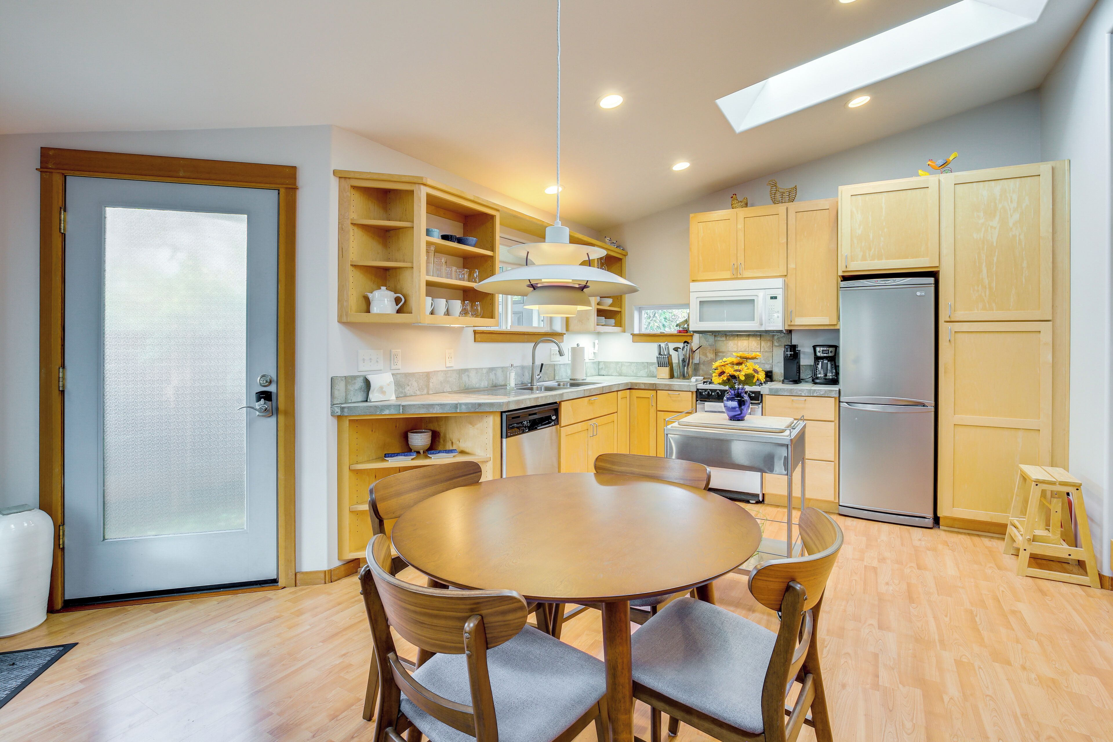 A modern kitchen with wooden cabinets, a stainless steel refrigerator, and a dining area with a round table and chairs.