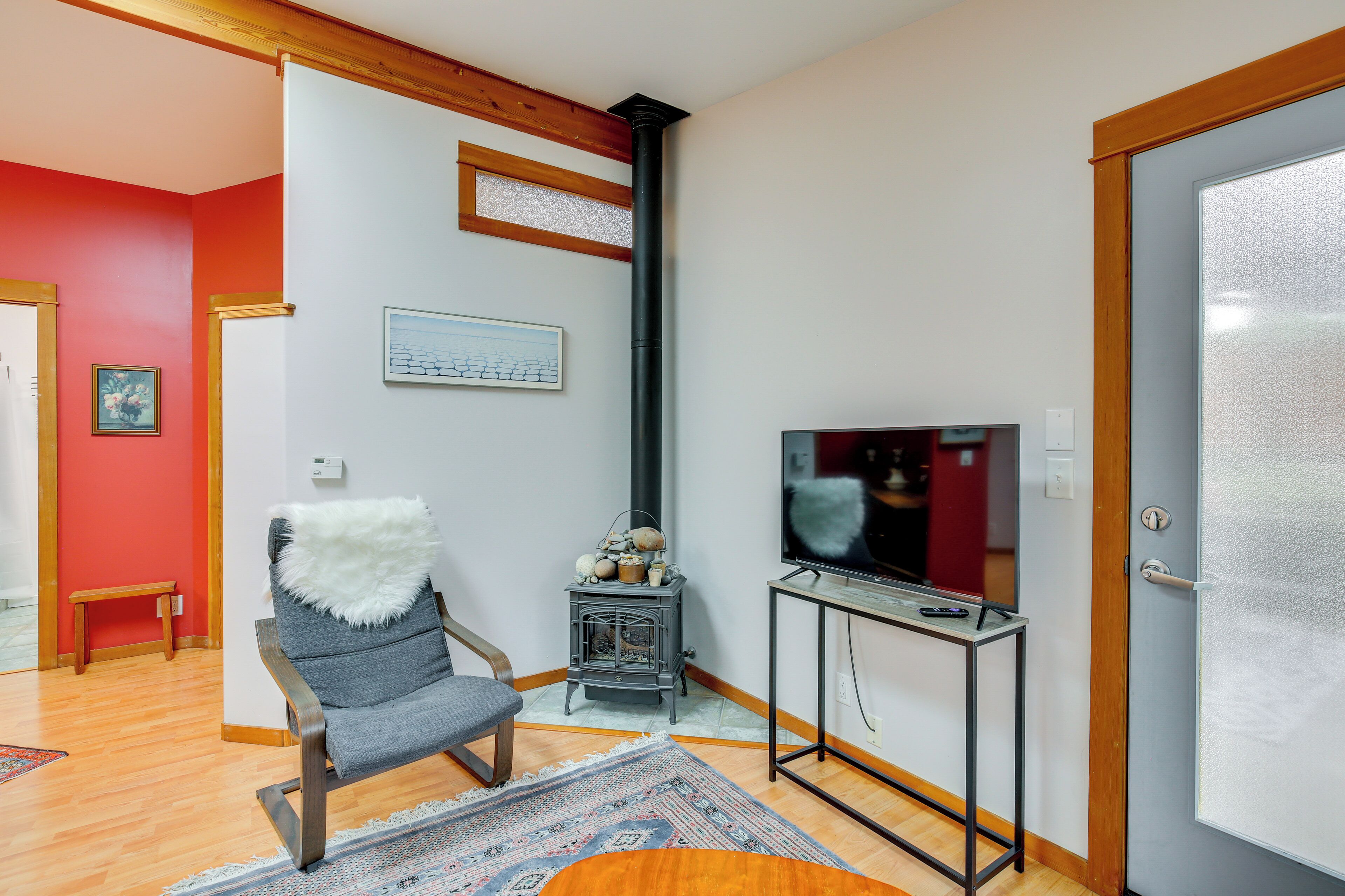 A living room with a wooden floor, a grey chair, a television on a black stand, a small heater, and a door with frosted glass.