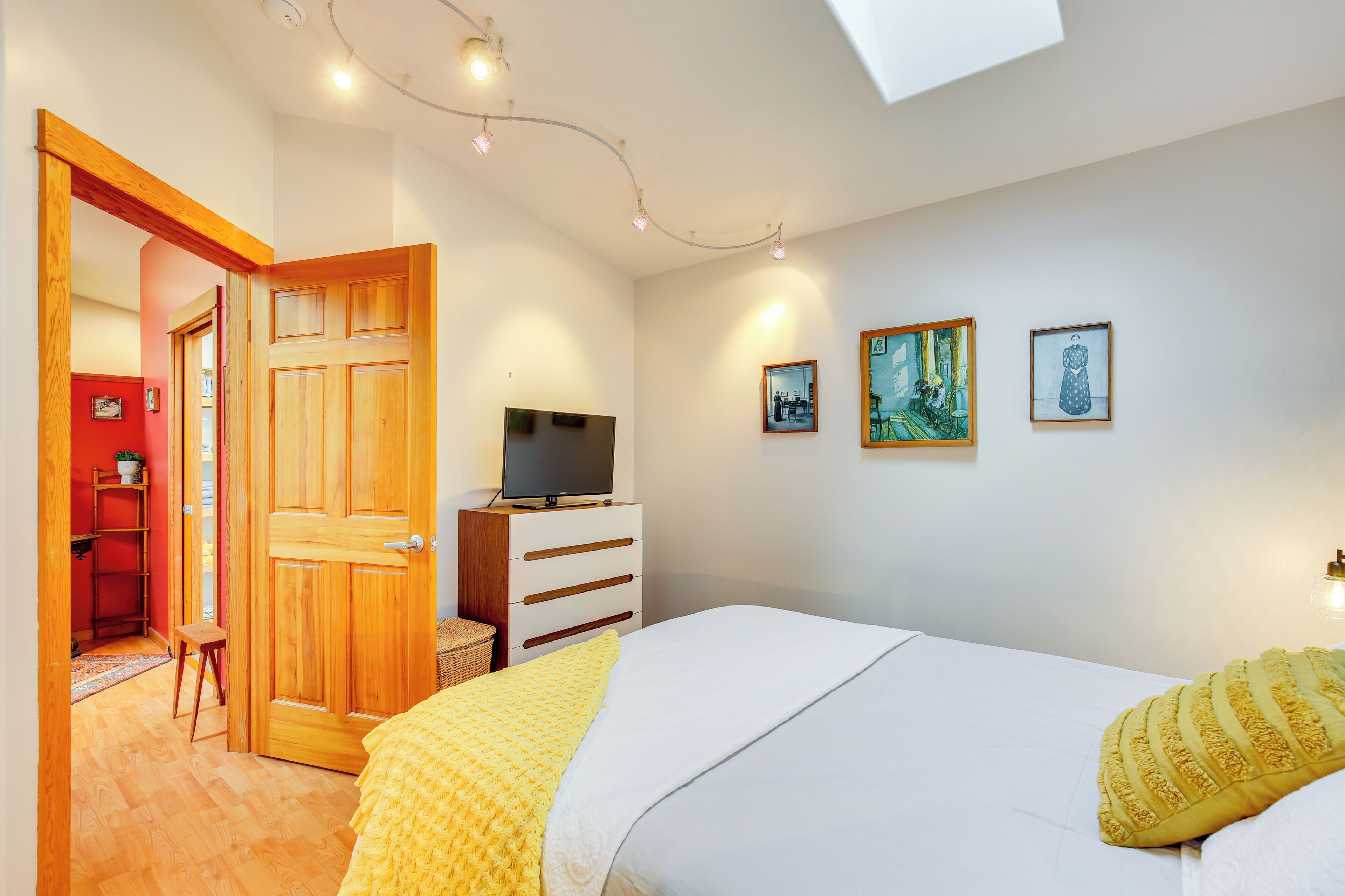 Een slaapkamer met een bed, een dressoir, een televisie en kunst aan de muur.